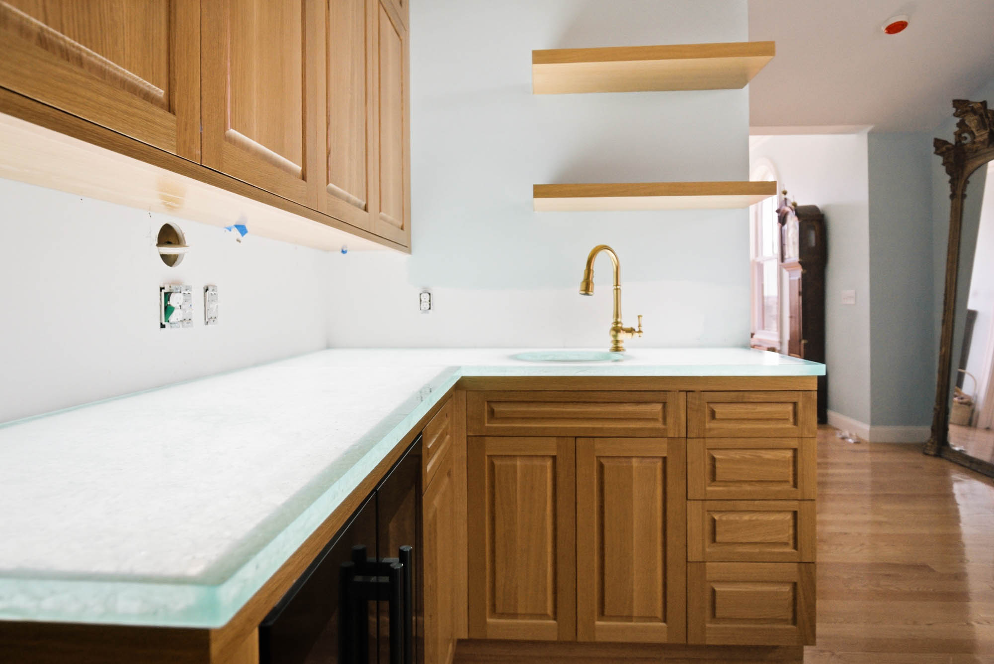 Butler's pantry wide view — glass counter, wine fridge area, brass faucet, floating shelves - kitchen plumbing