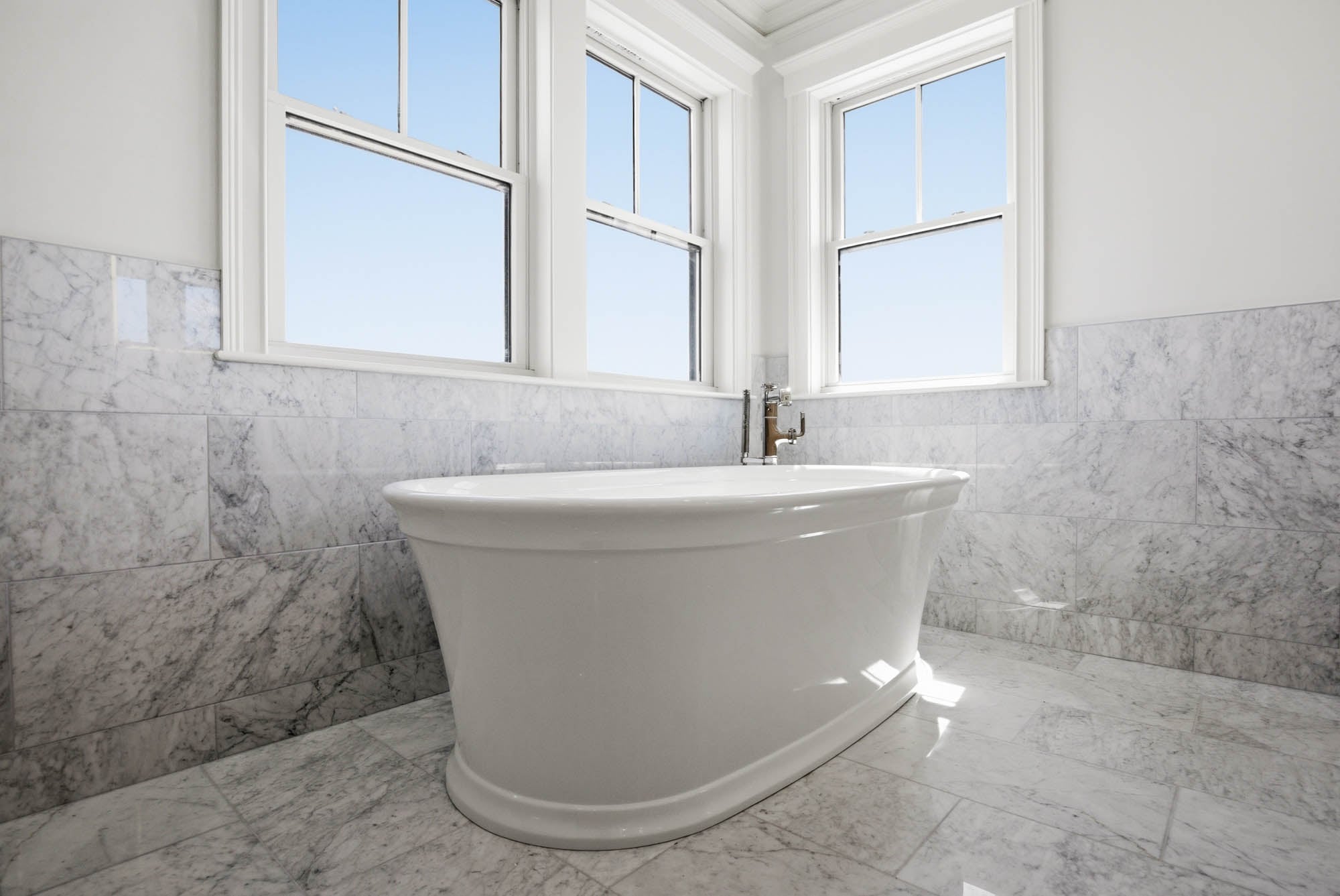 Freestanding soaking tub with polished nickel tub filler, marble tile surround, three windows - Essex County MA