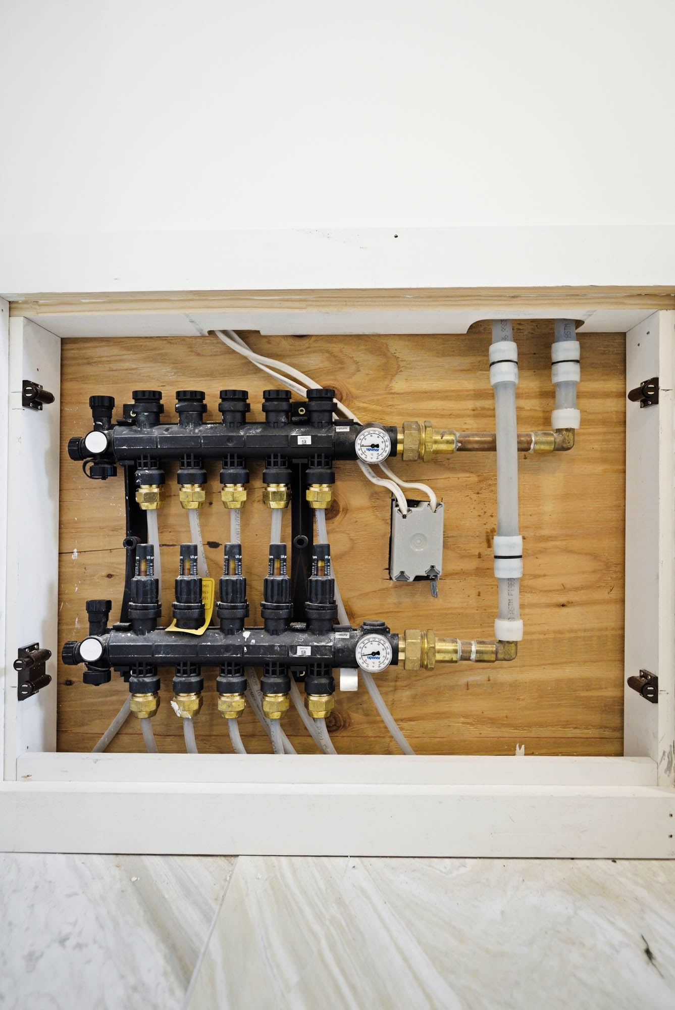 Radiant heat manifold mounted in wall cabinet with supply/return lines and gauges - hydronic heating