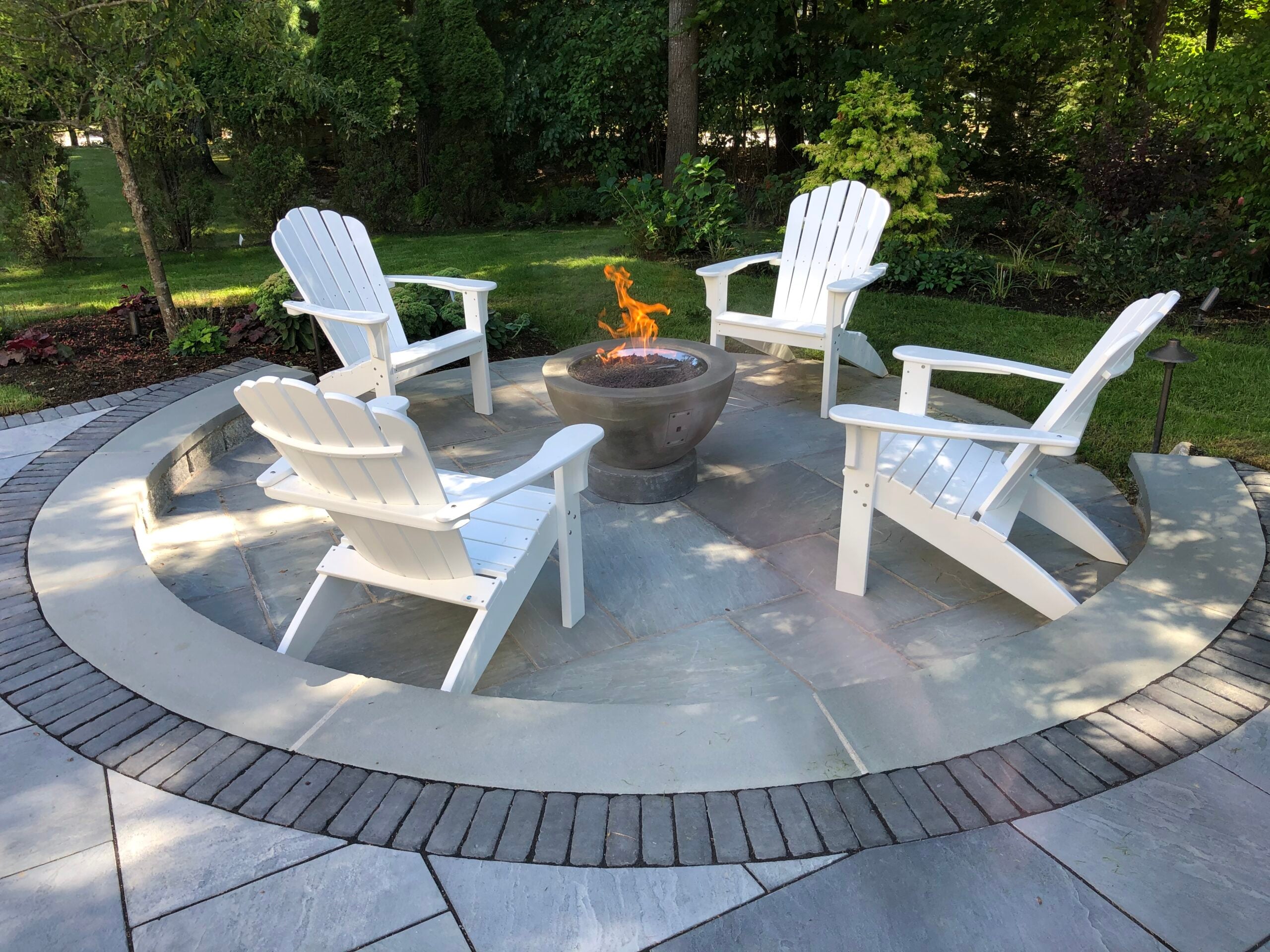 Outdoor gas fireplace lit with chairs around it, wide view of ECPH outdoor living installation